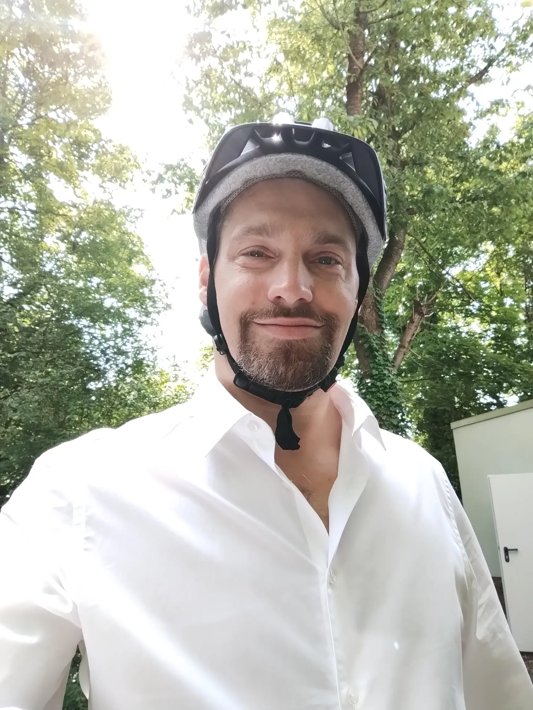 Marco Müller im weißen Hemd mit Fahrradhelm, umgeben von Bäumen – startklar für Termine in Hannover